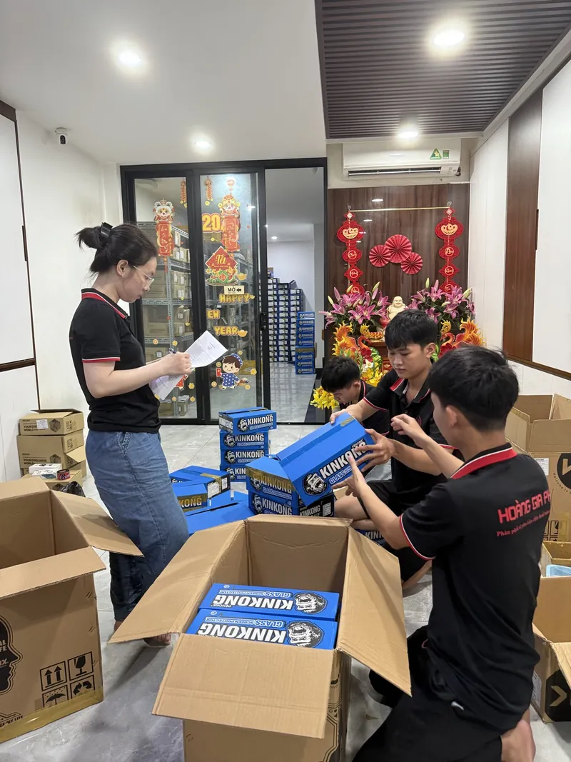 Nhân viên Hoàng Gia PK mặc đồng phục đen kiểm thùng kính cường lực KingKong, một bạn cầm phiếu đối chiếu